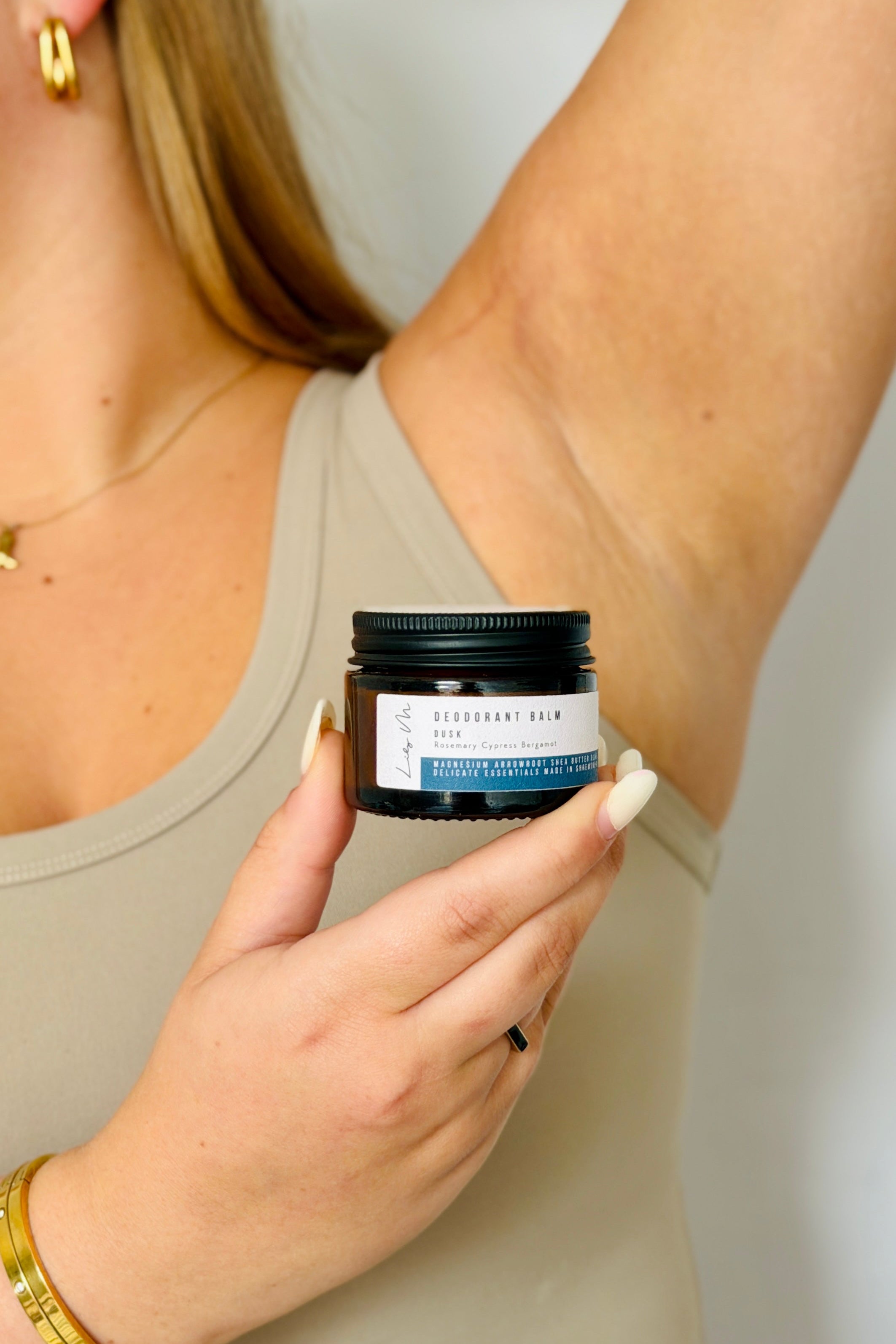 Woman applying deodorant balm to her arm with a jar of balm in her hand.