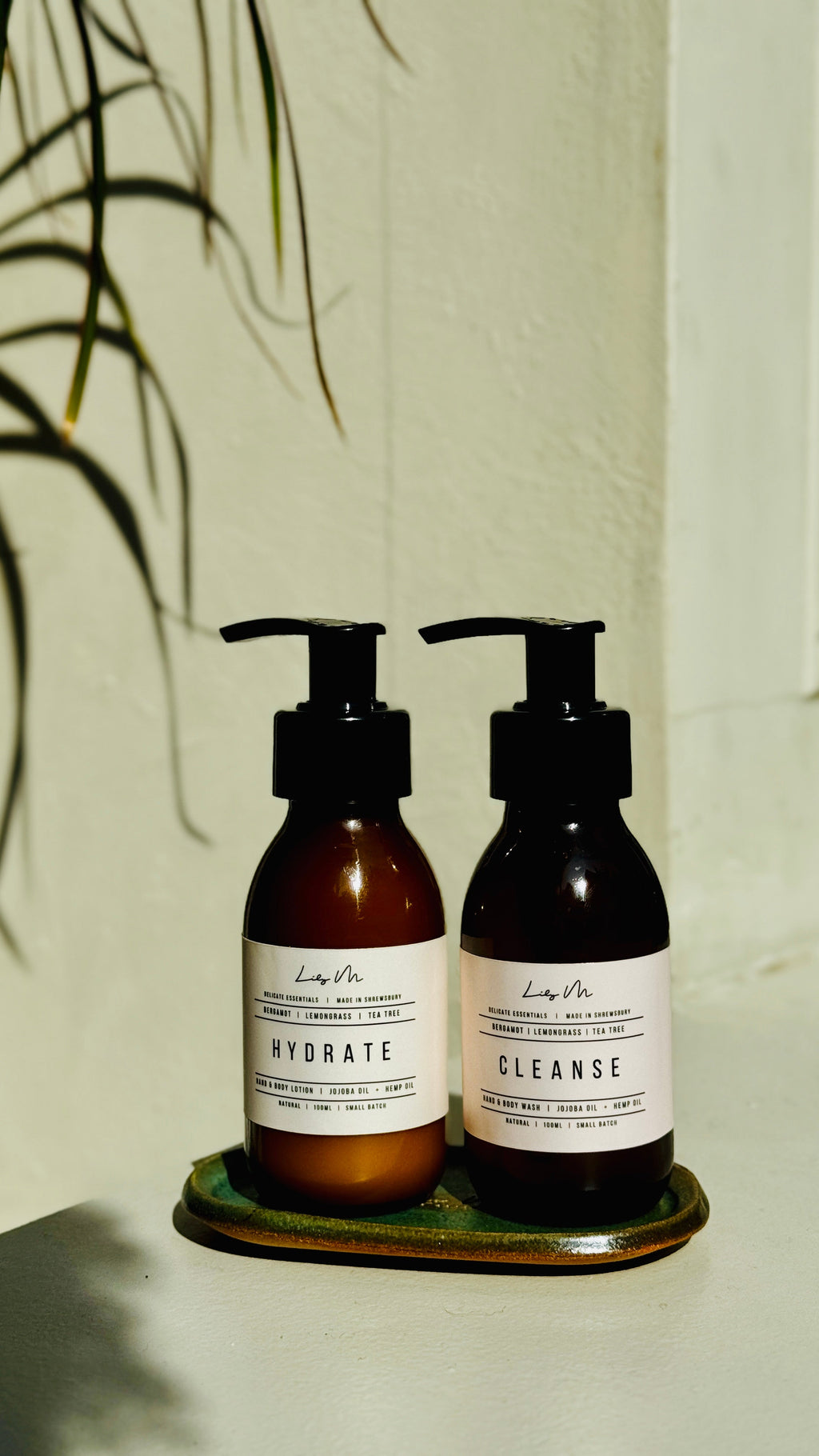 Two brown bottles with pump dispensers labeled 'Hydrate' and 'Cleanse' on a white surface with a plant in the background.