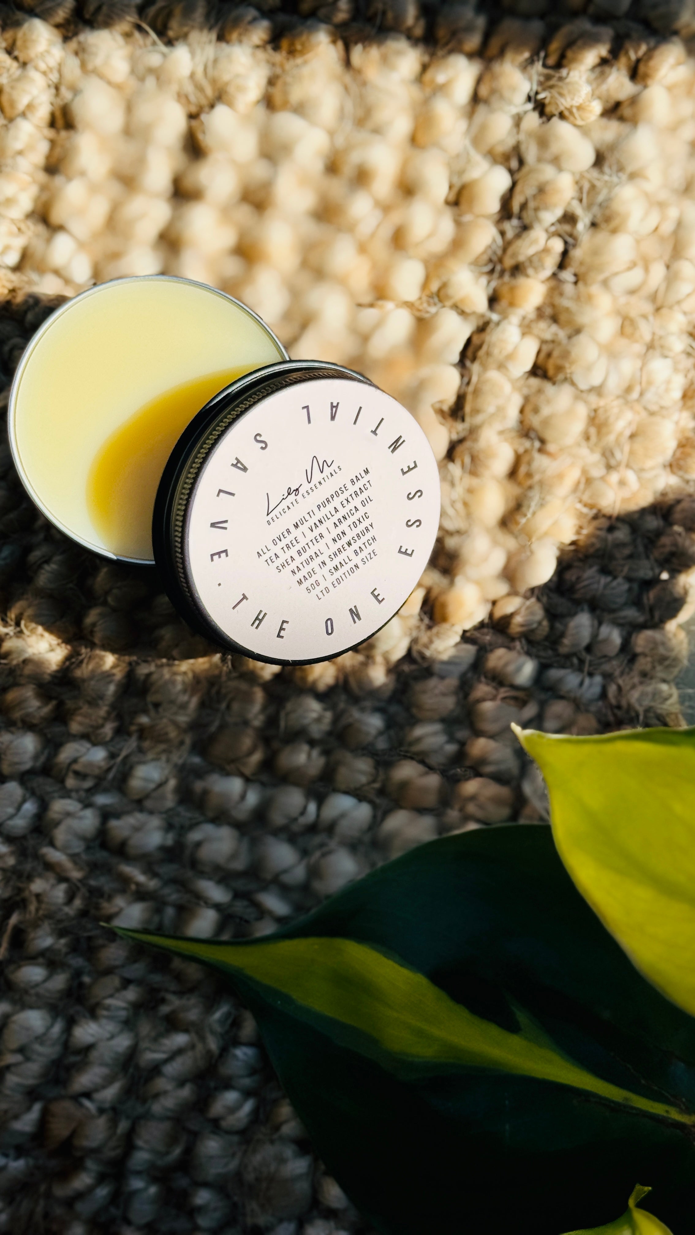 multi purpose balm with lid off showing the colour of the balm with a green plant in the bottom right hand corner