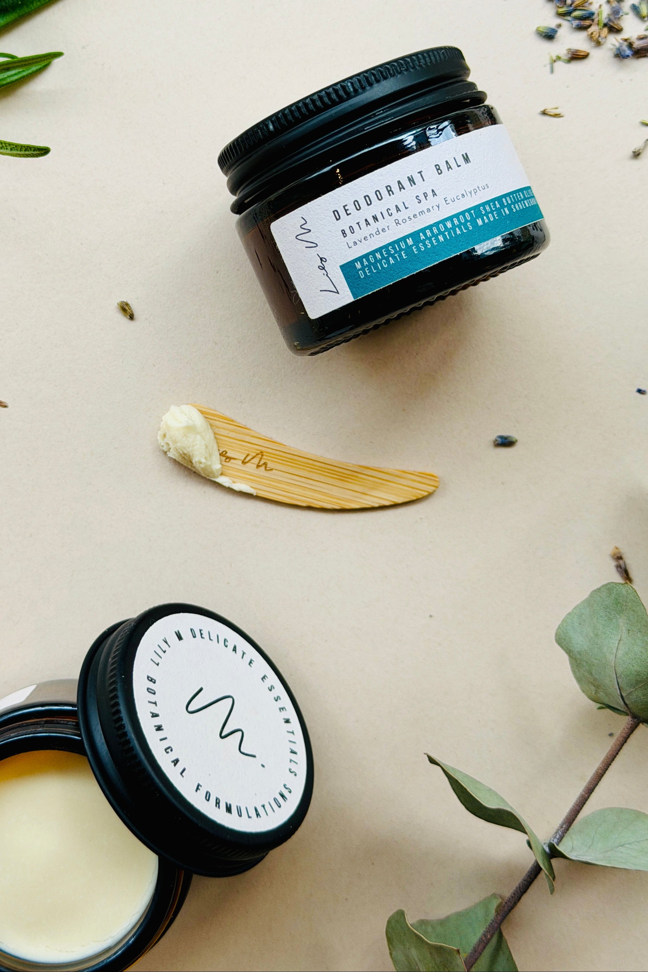 Deodorant balm jar with a label on a light background with herbs and leaves.