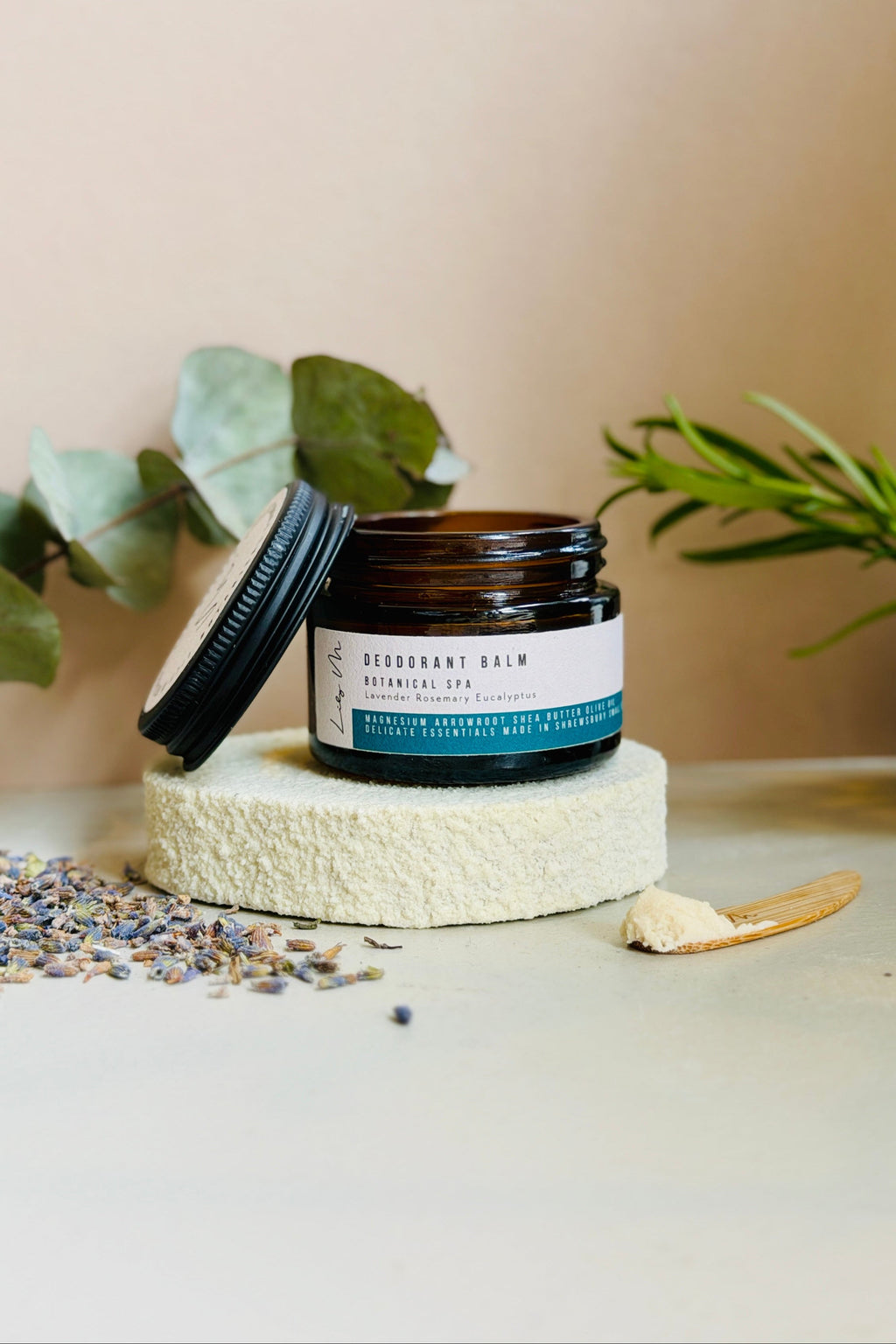 Jar of deodorant balm on a textured surface with plants in the background