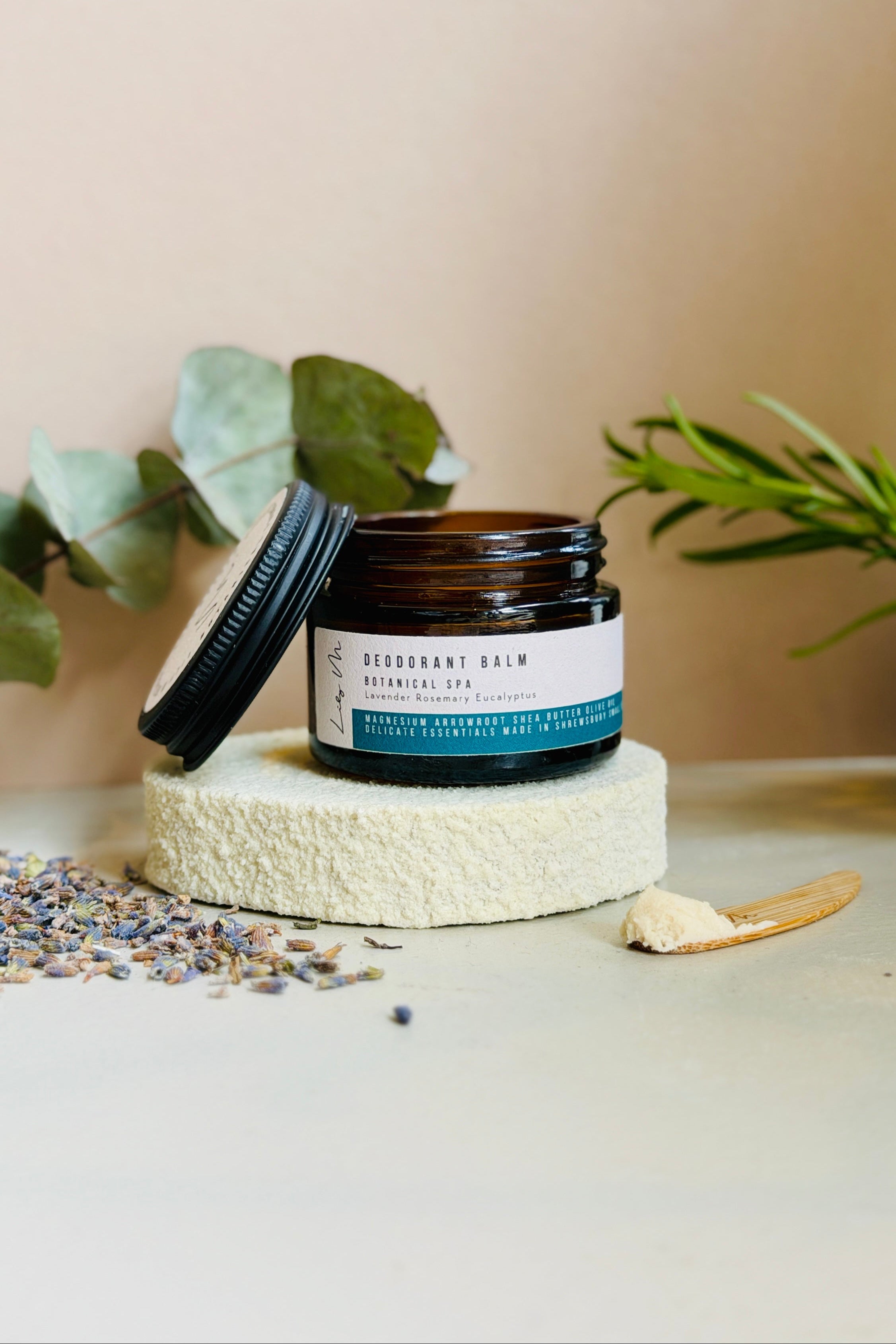 Jar of deodorant balm on a textured surface with plants in the background