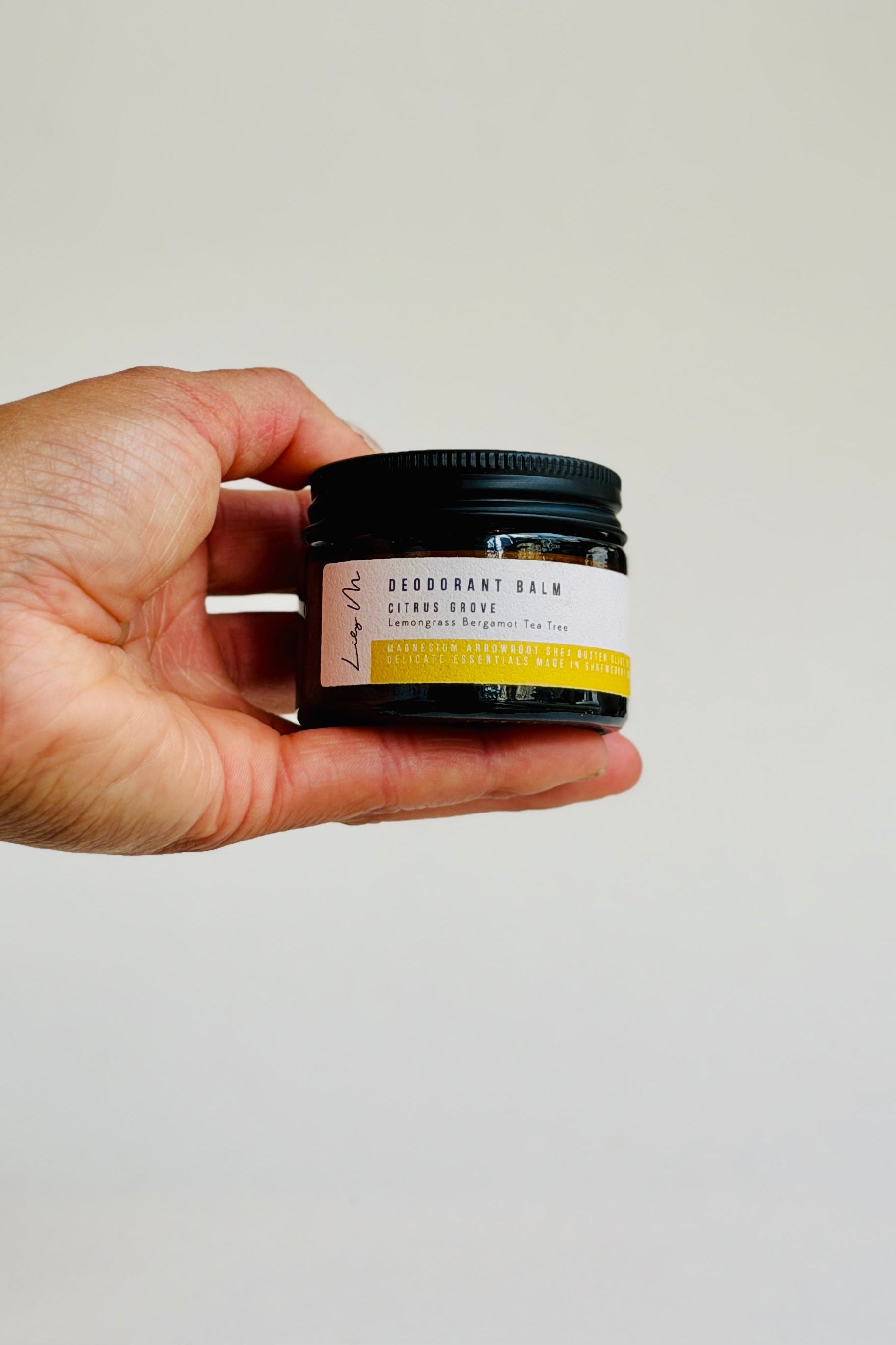 Hand holding a small jar of deodorant balm against a plain background