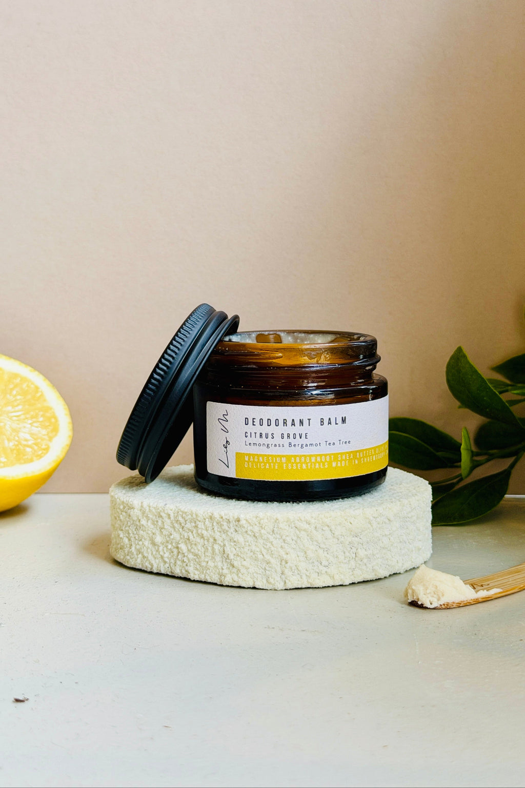 Jar of deodorant balm on a white surface with a lemon and green leaves in the background.