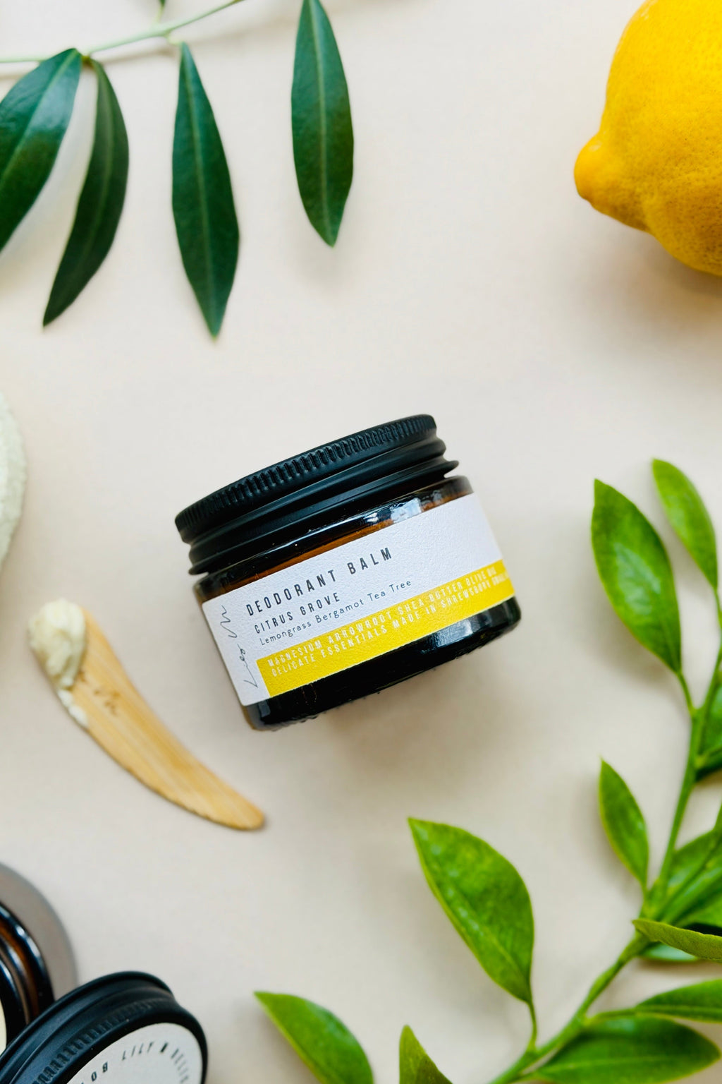 Jar of balm with a label surrounded by green leaves and a lemon on a light background