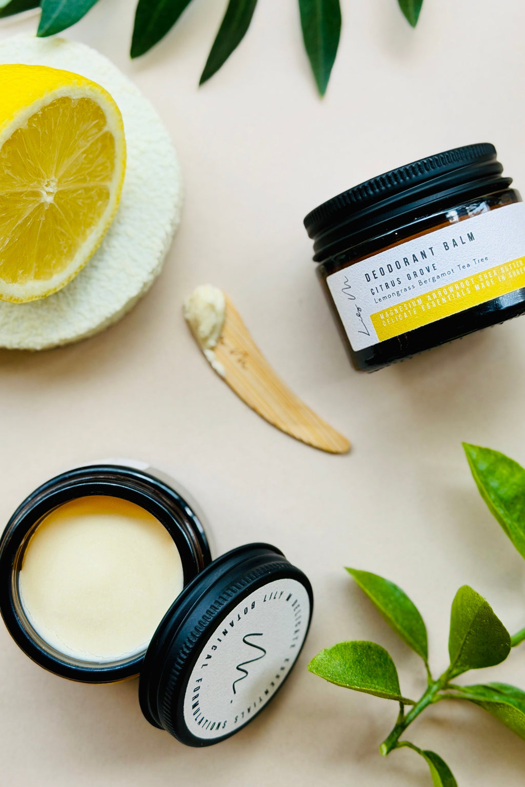 Two open black containers of skincare product with a lemon and leaves on a light background