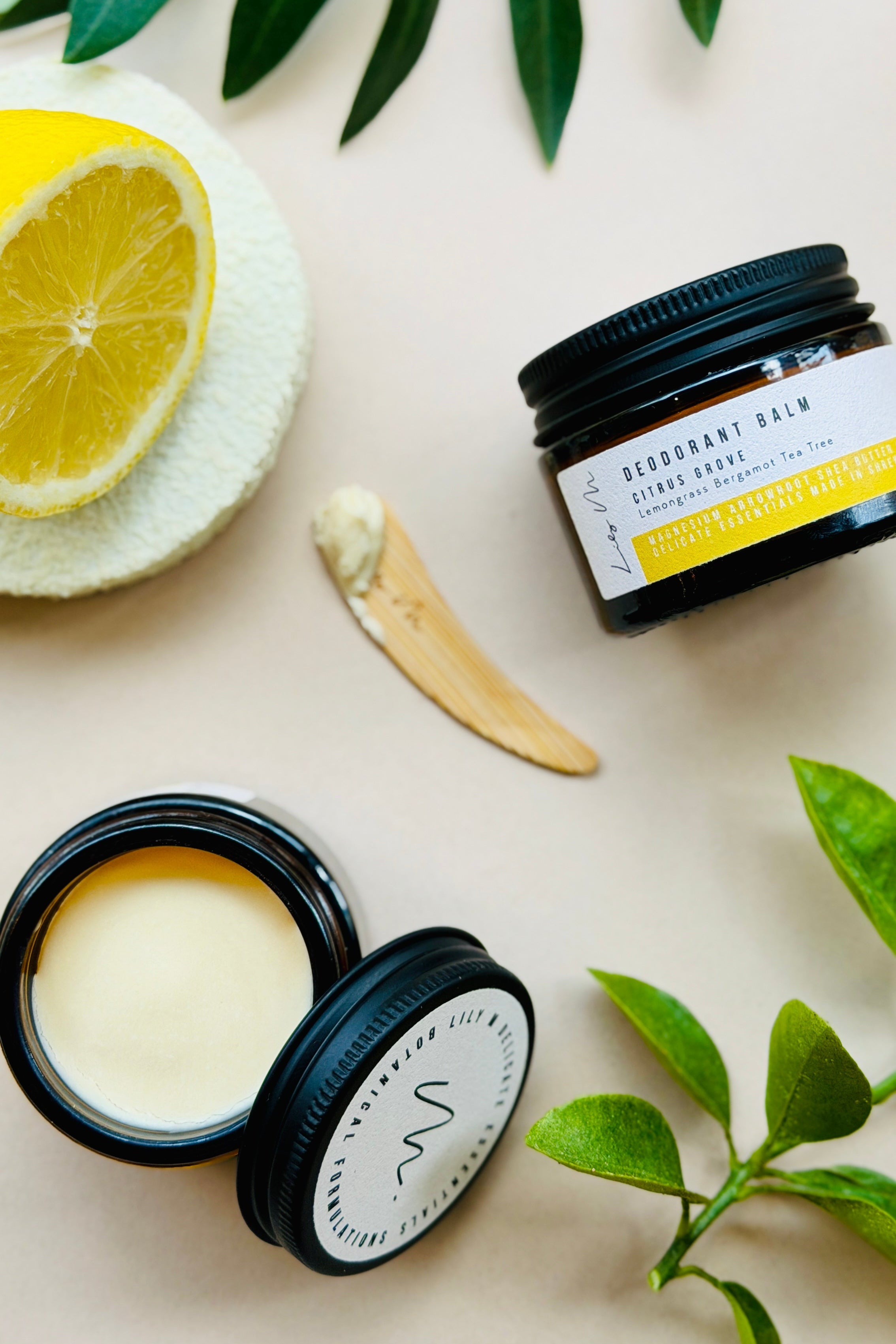 Two open black containers of skincare product with a lemon and leaves on a light background