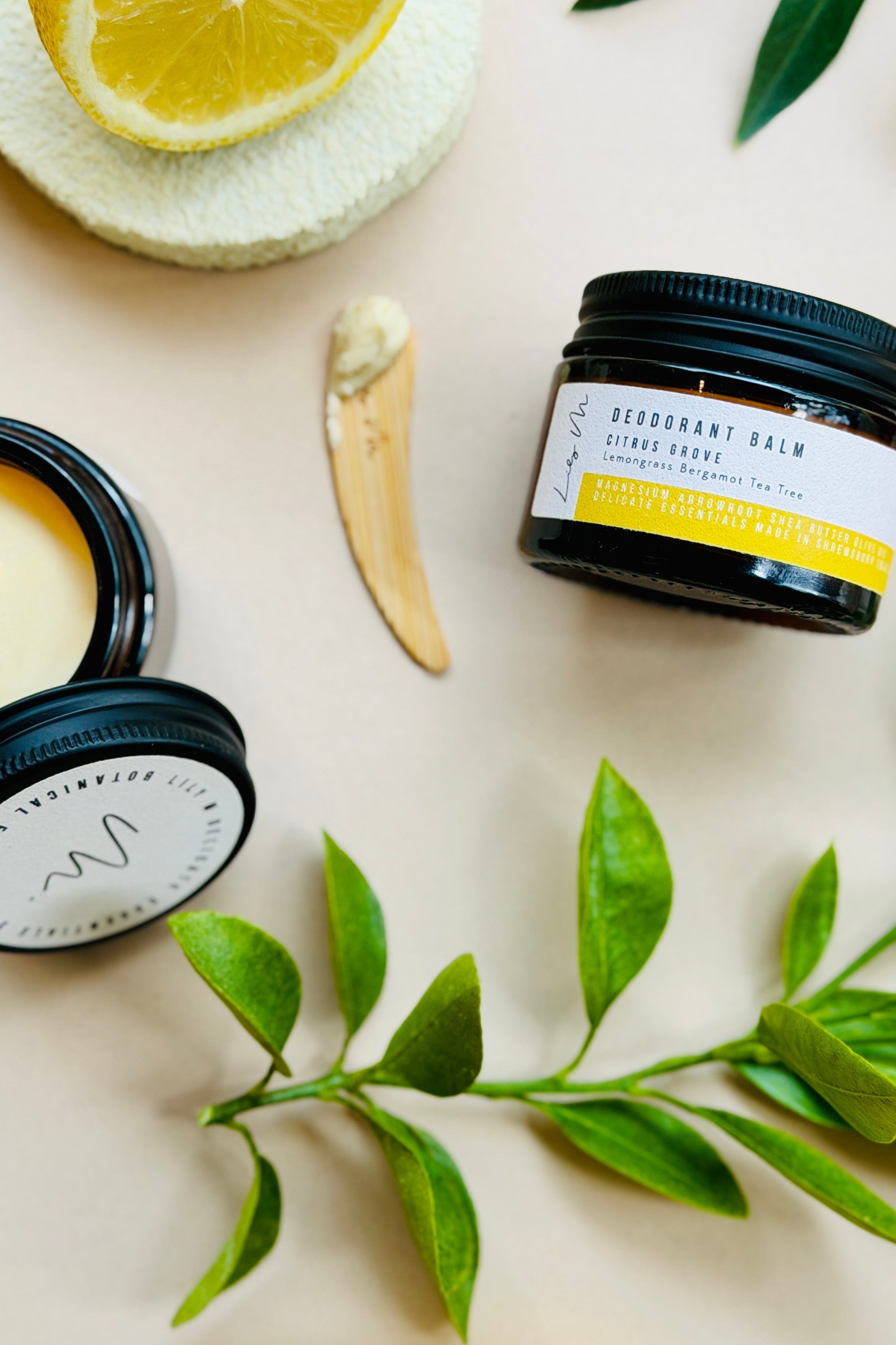 Deodorant balm jar with lemon slices and leaves on a light background