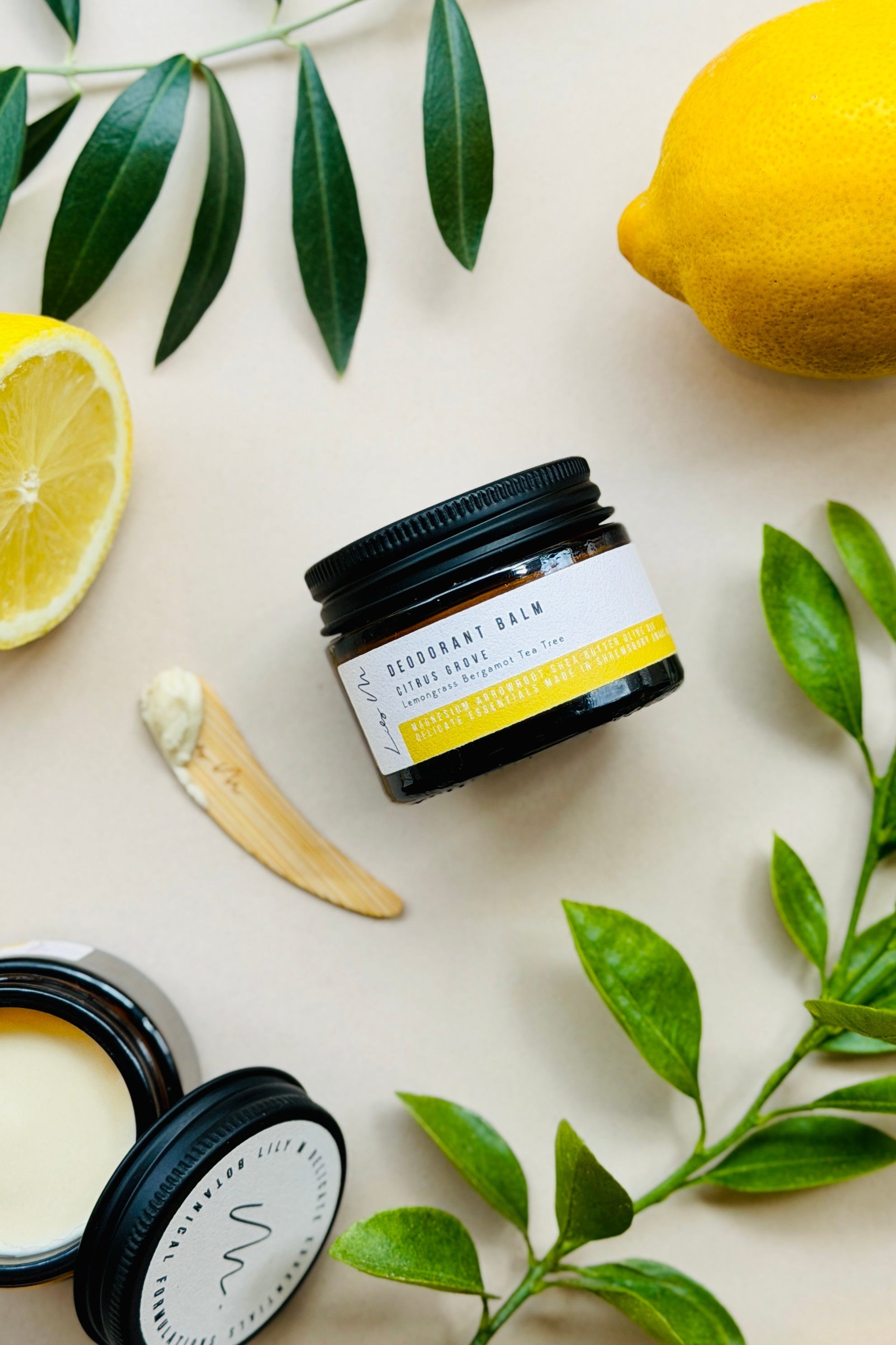Jar of deodorant balm with lemons and green leaves on a light background