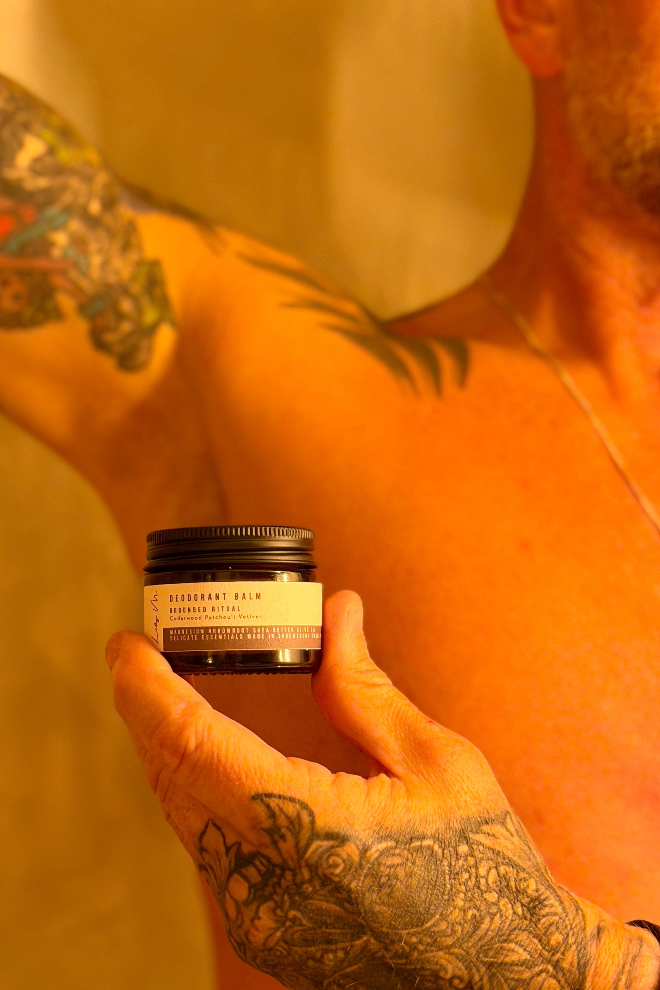 Man with tattoos holding a jar of deodorant against a neutral background