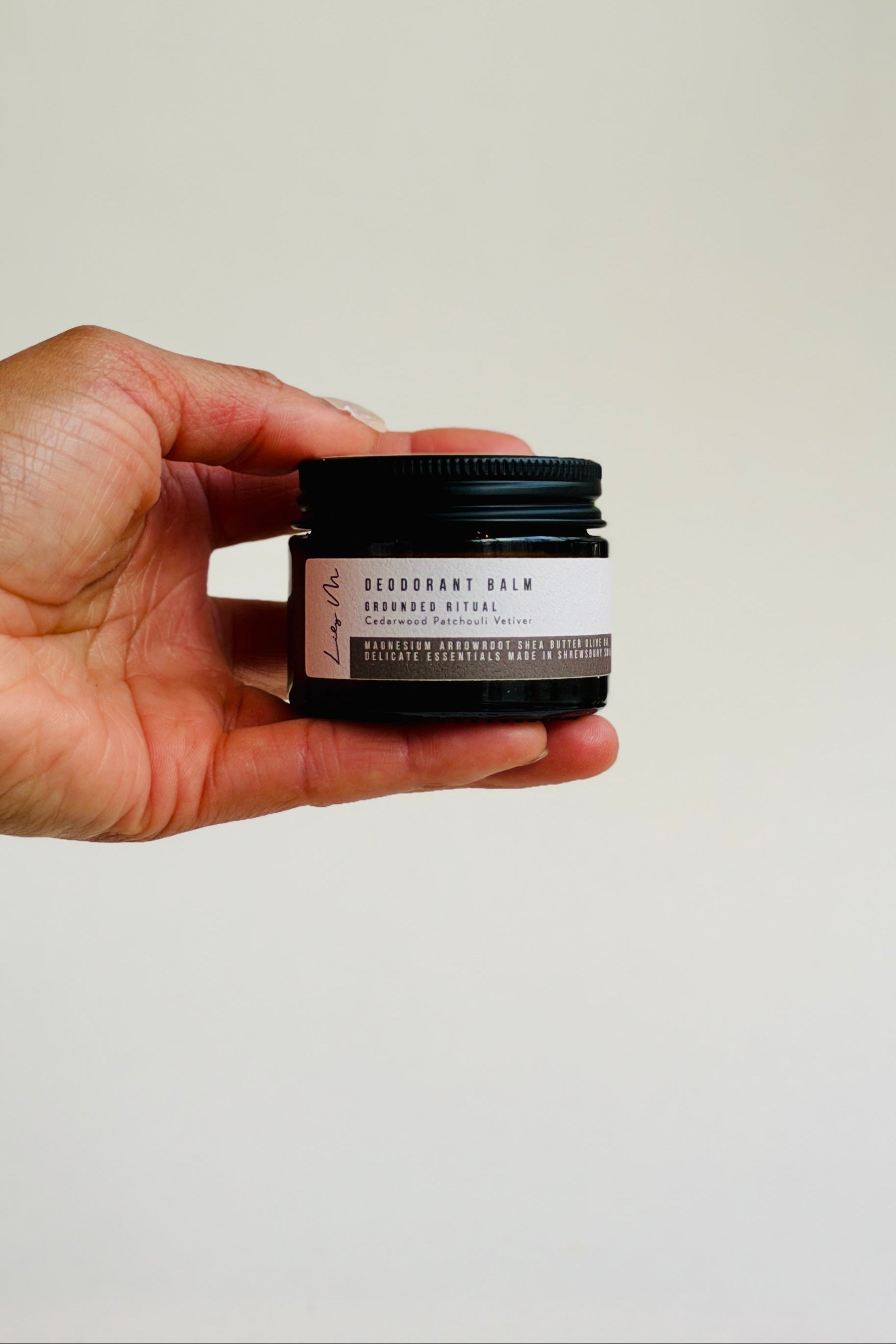 Hand holding a small jar of deodorant cream against a plain background