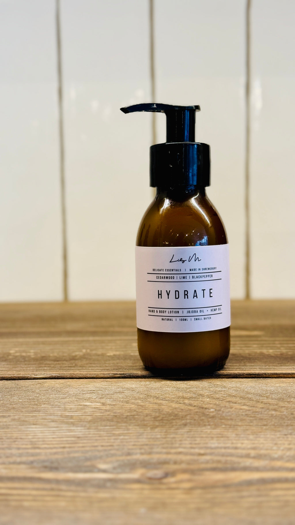 travel size 100ml hand and body lotion in a small amber glass bottle with a black pump