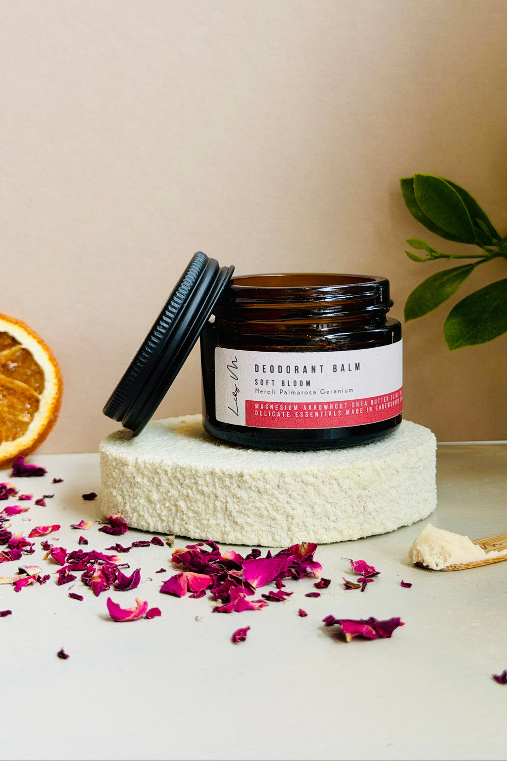 Jar of deodorant balm on a white stand with an orange and dried flowers on a beige background