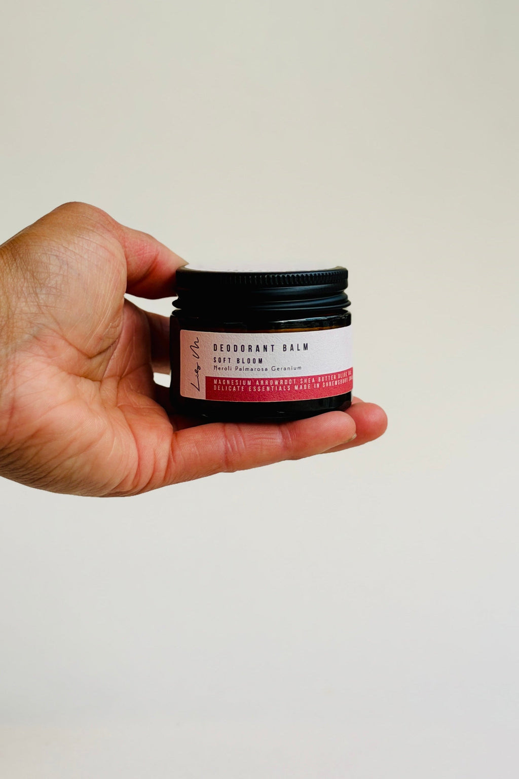Hand holding a small jar of deodorant cream against a plain background